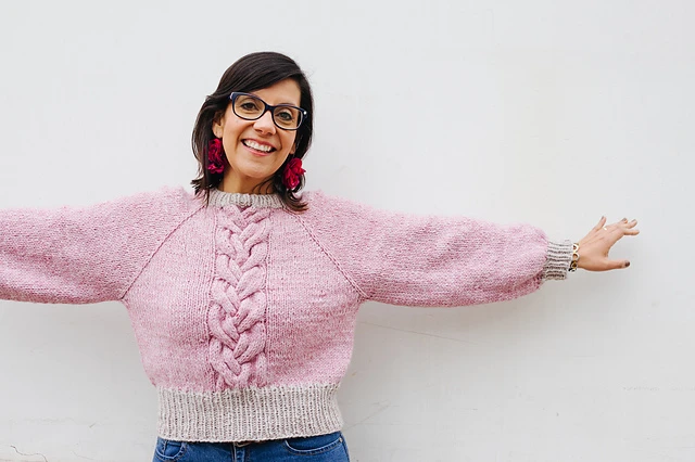 Fotografía de una mujer mostrando el sweater Venus con sus brazos abiertos. El sweater está tejido en punto jersey y tiene una trenza compleja en el centro.